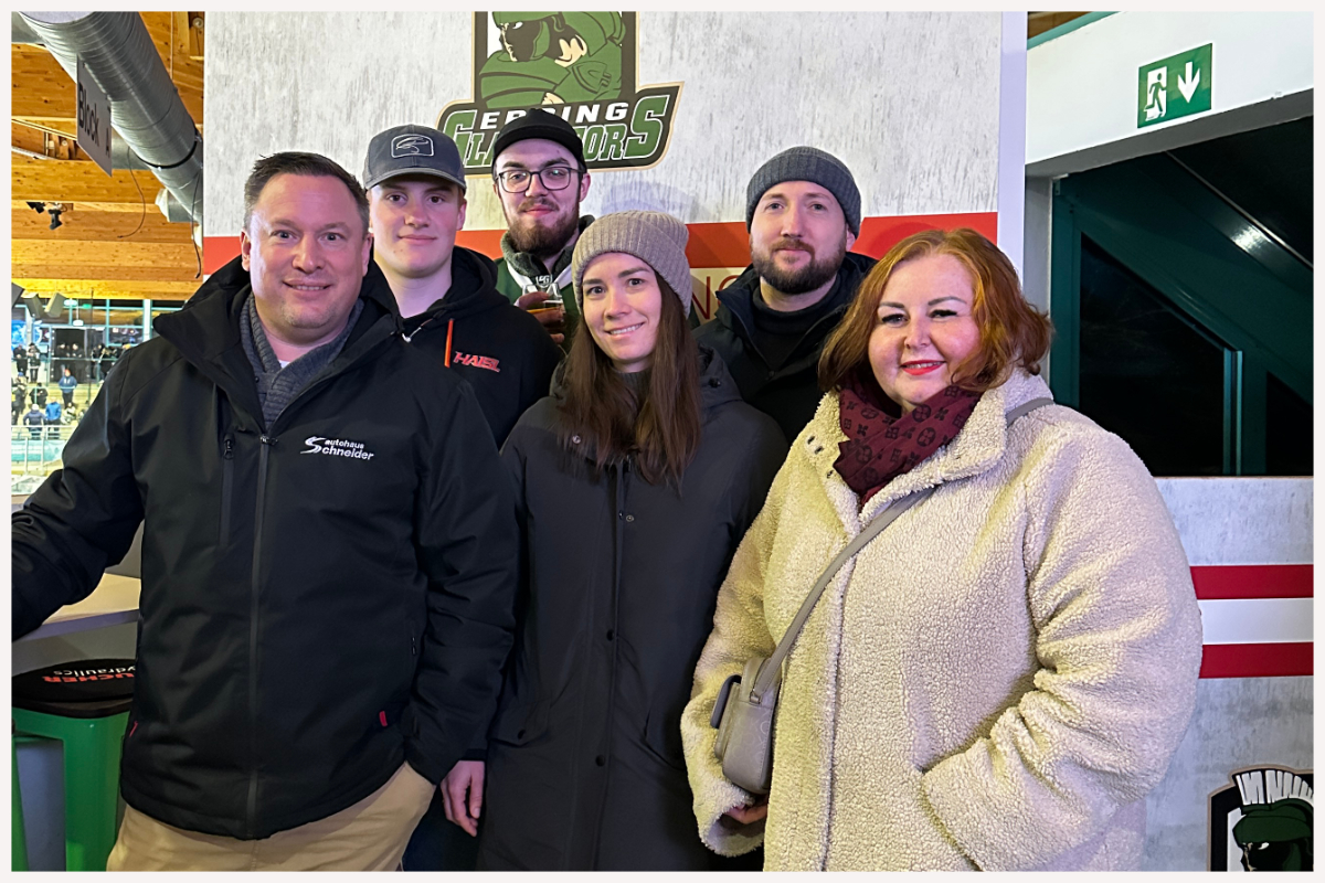 Sechs glückliche Spielgewinner stehen vor dem Logoschild