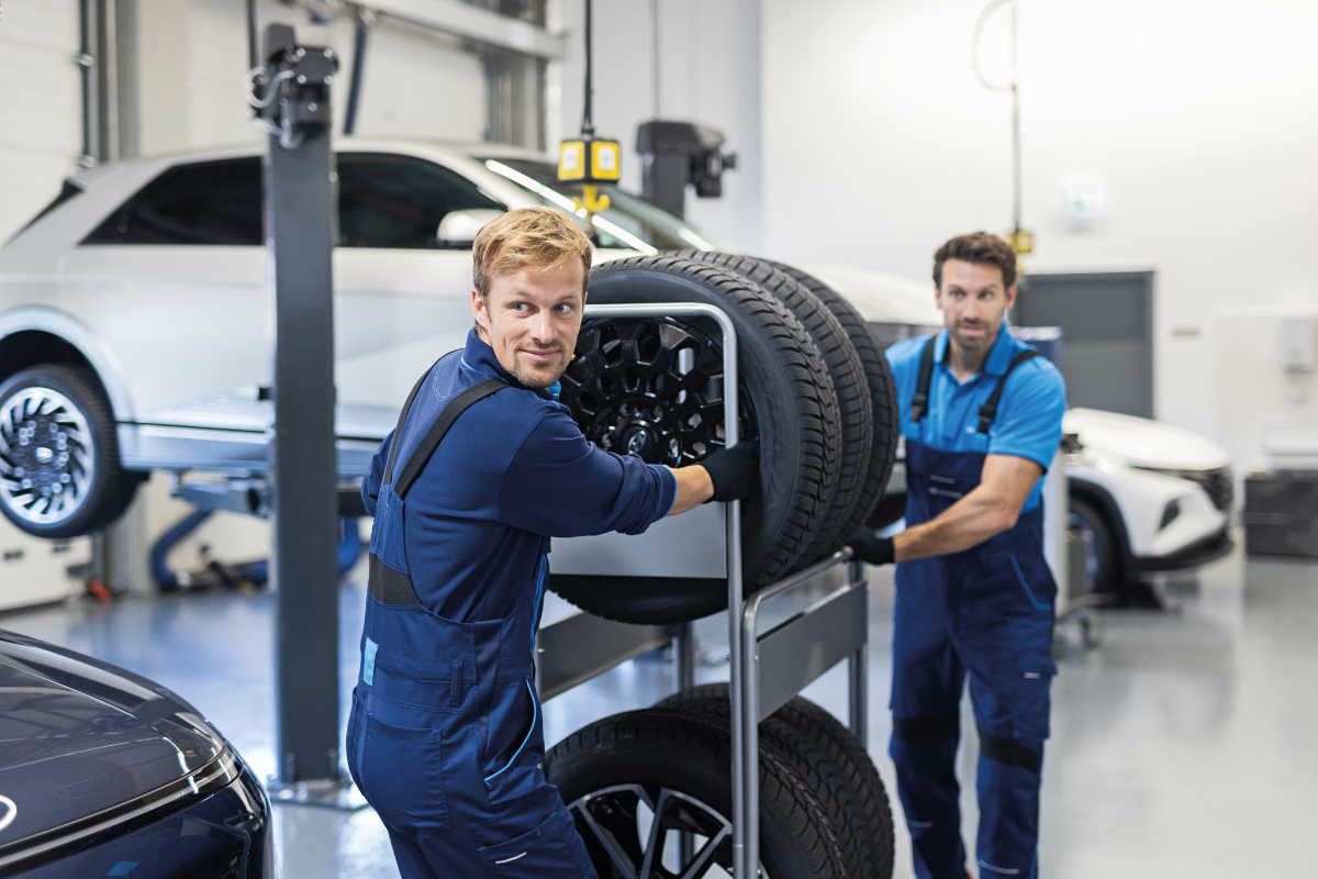 zwei Manner schiben ein Regal mit Reifen