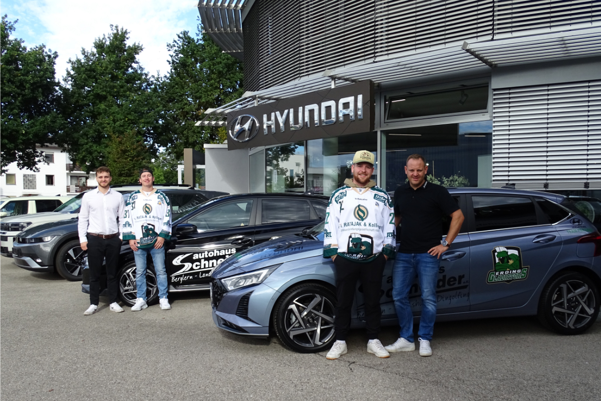 Zwei Spieler der Erding Gladiators und die zwei Geschäftsführer des Autohauses, die neben Autos stehen.