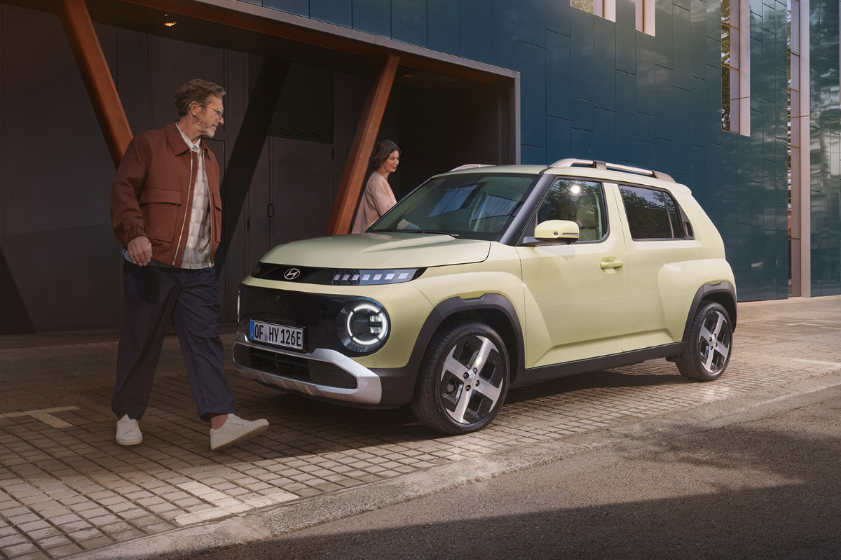 ein Hyundai Inster steht vor Gebäude und daneben sind ein Mann und eine Frau