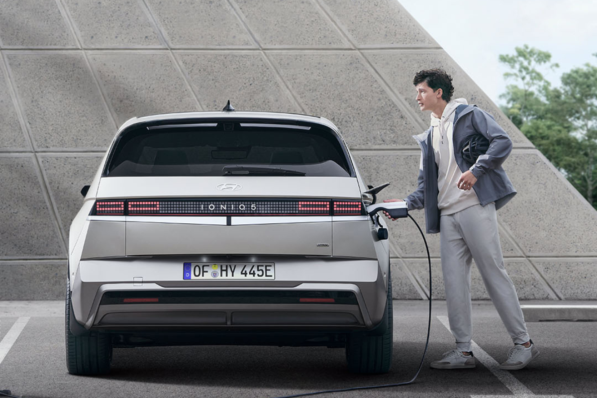 Ein weißer Hyundai IONIQ 5 steht an einer Ladestation, und ein Mann lädt das Auto