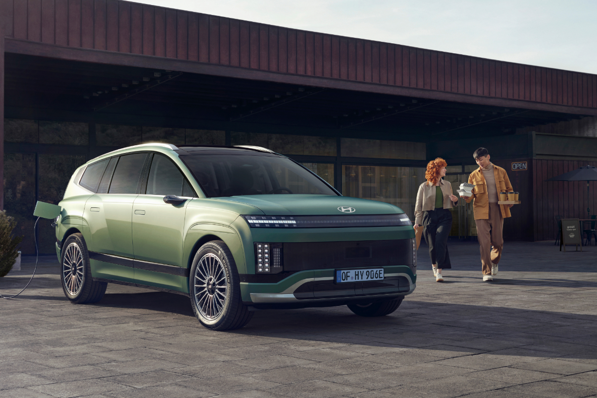 Ein Hyundai IONIQ 9 steht vor einem Café. Ein Mann und eine Frau halten Kaffee in der Hand und gehen auf das Auto zu